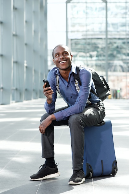 happy business man waiting at station with luggage and cellphone