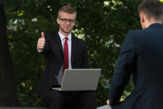 公園のベンチで外でタブレットPCを使用して幸せなビジネスの男性