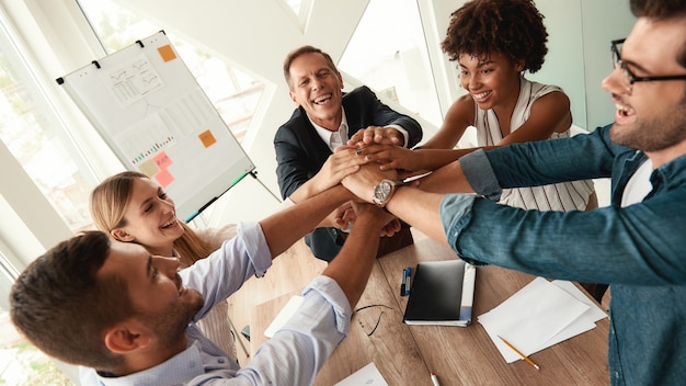 Happy business people holding hands together while sitting at the office table. Teamwork. Success