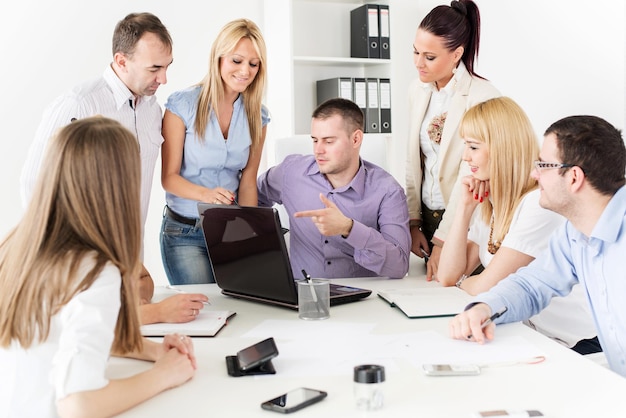 Счастливые деловые люди в офисе обсуждают проект на ноутбуке на встрече.