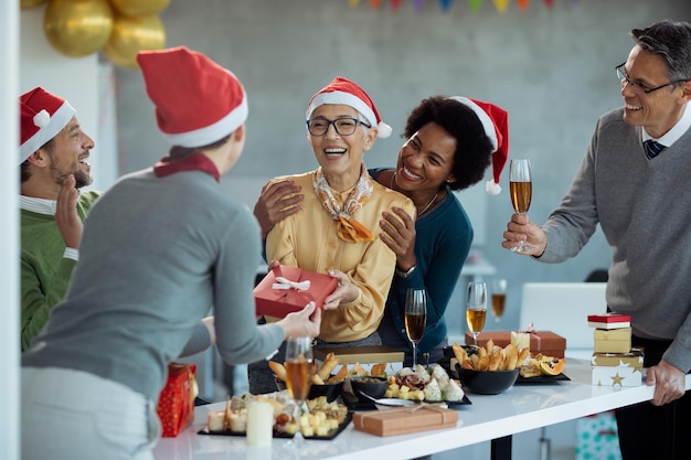 Happy business people surprising their colleague with a gift on Christmas party in the office