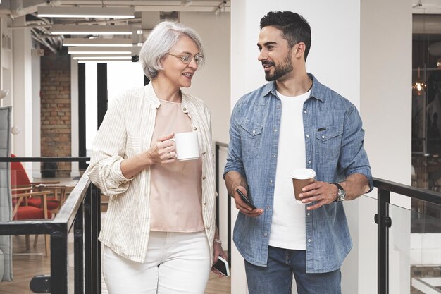 Happy business people take break with hot drinks stand in office talking Startup concept