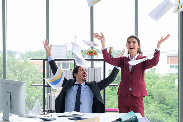 La squadra felice di affari celebra il lancio di documenti di successo nella sala riunioni dell'ufficio