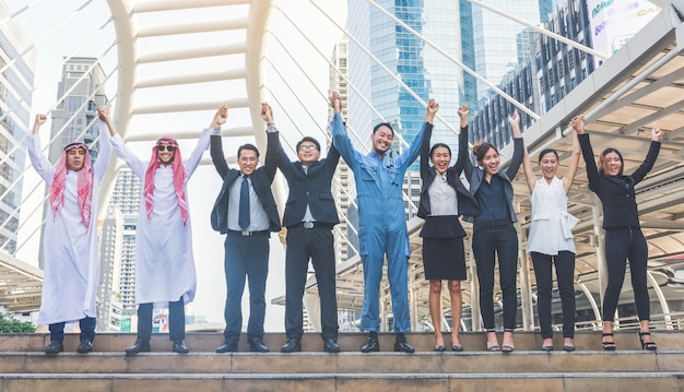 Happy business team making high hands in city background 