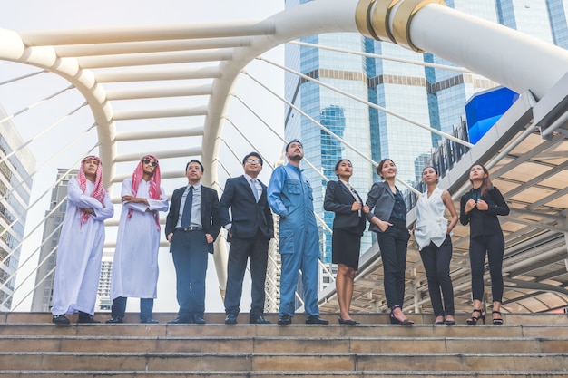 Happy business team making high hands in city background 