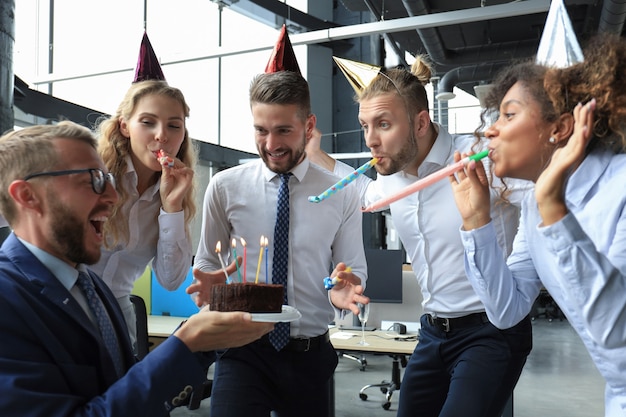 Happy business team with birthday cake are greeting colleague at office party.