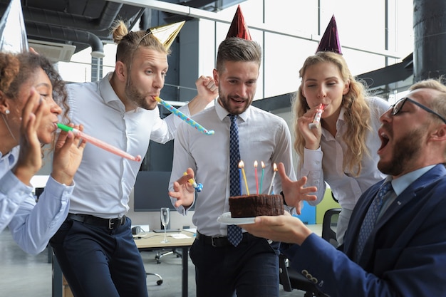 Happy business team con torta di compleanno saluta il collega alla festa in ufficio.