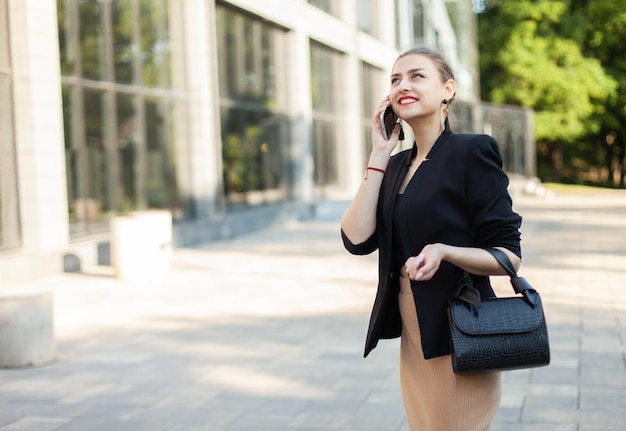 Happy business woman office worker in business clothes talking on the phone outdoors