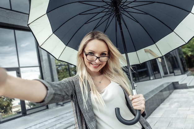 幸せなビジネス女性は、営業所の背景に傘を開きます。自分撮りポートレート
