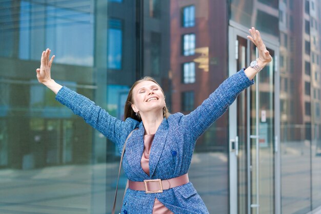 オフィスに対して屋外に立っている間親指を現して幸せなビジネス女性