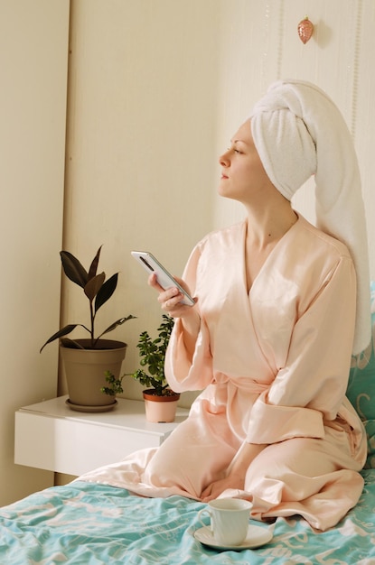 happy business woman with a towel on her head lies in bed in pajamas in a cozy home with notebook.