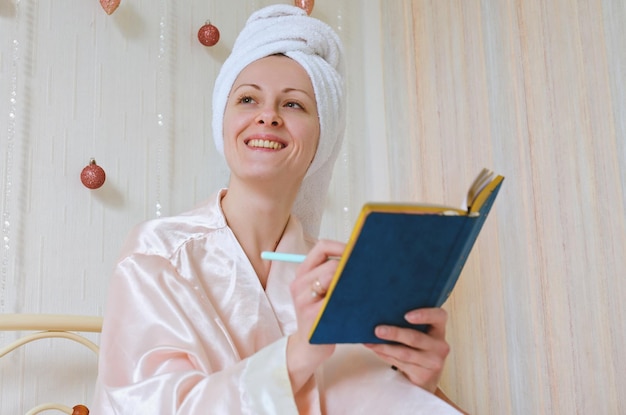 happy business woman with a towel on her head lies in bed in pajamas in a cozy home with notebook.