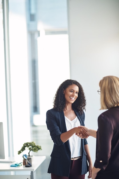 Photo happy business women shaking hands meeting and greeting in an office confident young professional talking to a manager about a promotion or job performance hr congratulating an ambitious employee