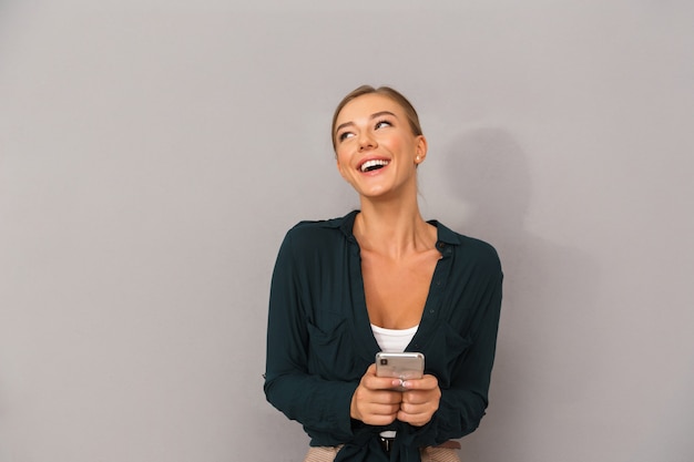 휴대 전화를 사용 하여 회색 벽 배경 위에 절연 포즈 행복 비즈니스 젊은 여자.