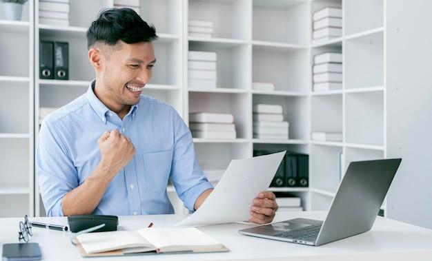 Happy businessman celebrating a win raised up hands in light modern workstation