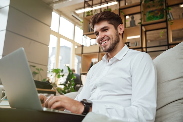 Счастливый бизнесмен, одетый в белую рубашку, сидя в кафе и используя ноутбук.