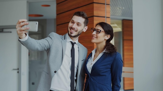 Happy businessman and his female colleague taking a selfie on smartphone camera for social media