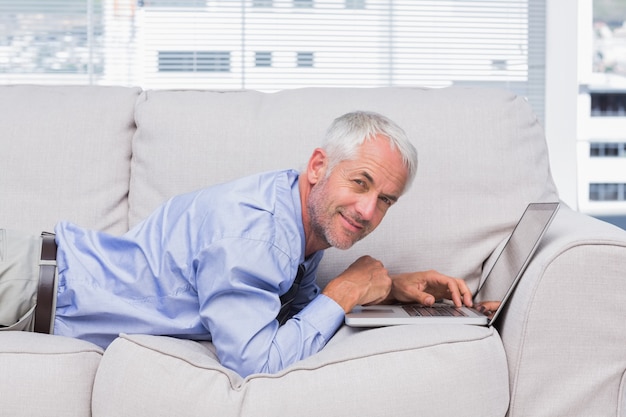 Happy businessman lying on sofa with laptop in the office