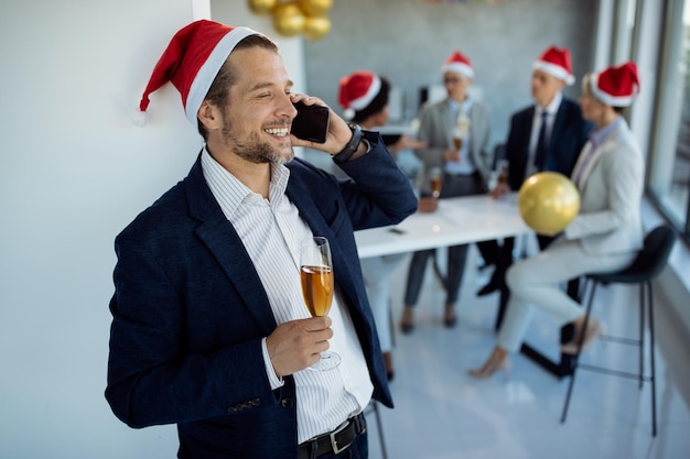 Happy businessman making a phone call while drinking Champagne on Christmas party in the office