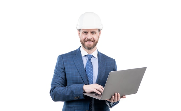 Счастливый бизнесмен в костюме и защитном шлеме, работающий на компьютере онлайн, изолированный от белого гибкого бизнеса