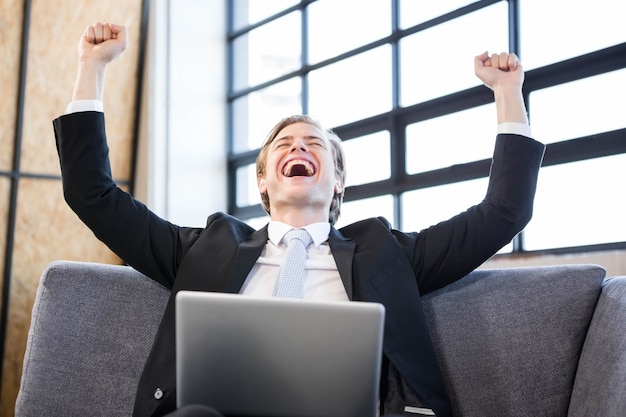 Happy businessman raising hands with excitement in front of laptop