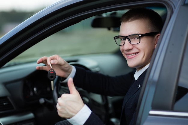 彼の新しい車のキーを示す幸せなビジネスマン