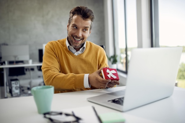 Happy businessman showing a present while talking to someone\
over laptop in the office