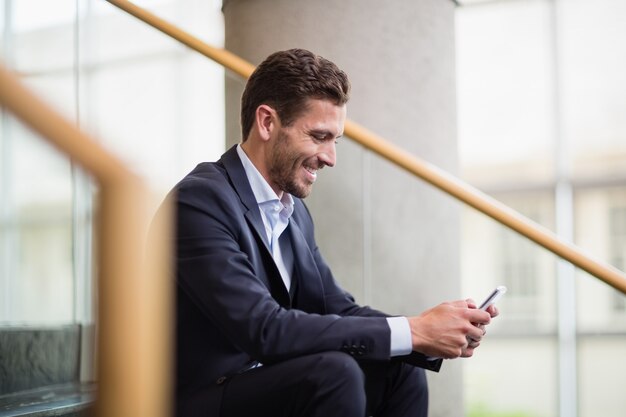 Photo happy businessman sitting on steps and using mobile phone