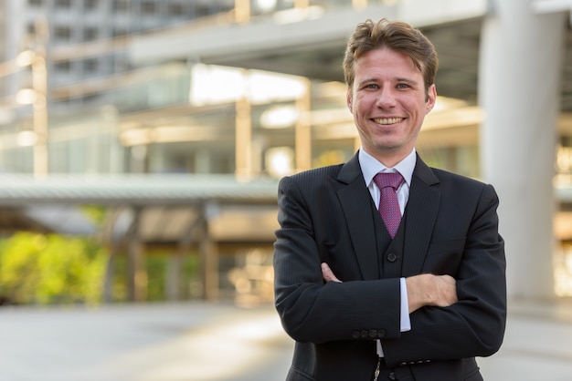 Happy businessman smiling with arms crossed in front of modern b