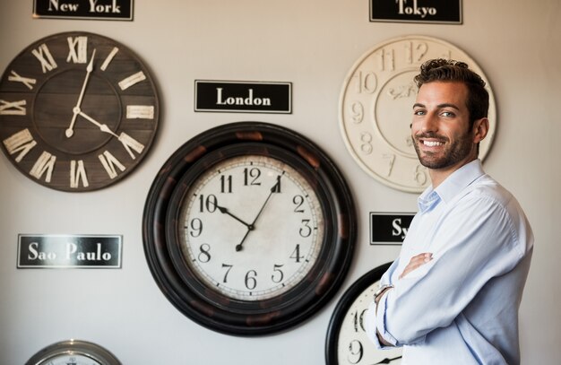 国際的な時計の壁の横に立っている幸せなビジネスマン