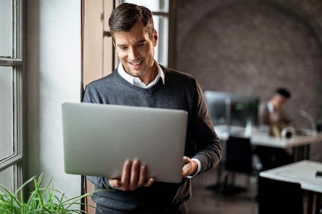 Photo happy businessman standing by the window and reading an email on a computer in the office