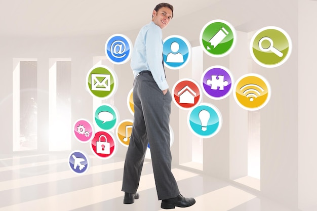 Happy businessman standing with hands in pockets against application icons in room