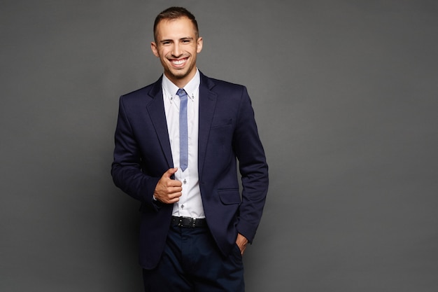 Happy businessman in suit isolated at dark background. A handsome young man in an official outfit posing