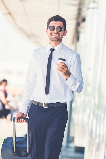 The happy businessman in sunglasses walk with a suitcase