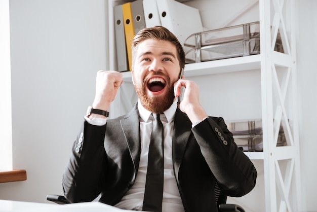 Happy businessman talking by phone and make winner gesture.