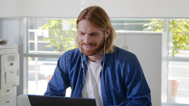 Happy businessman using earphones and having online meeting on laptop