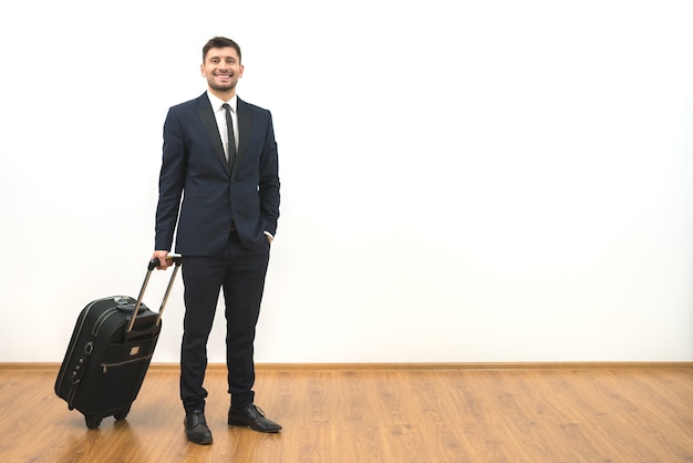 The happy businessman with a suitcase standing on the white wall background