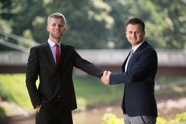Счастливые бизнесмены пожимают друг другу руки, стоя на открытом воздухе в парке