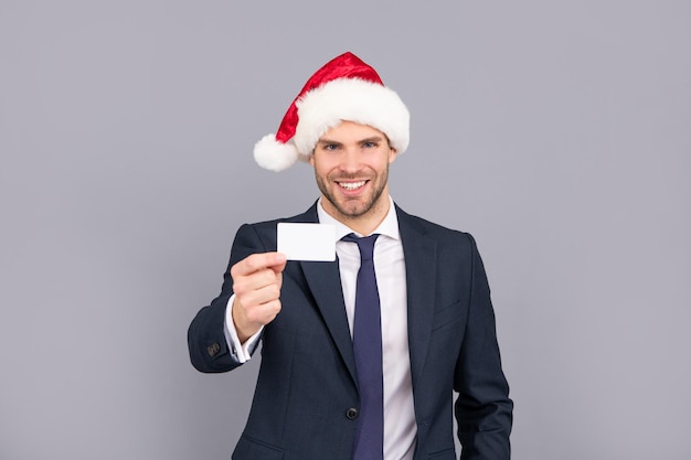 Happy businessperson guy wear santa hat hold debit card on grey background copy space membership