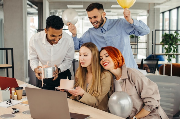 Happy businesswoman blowing out a candle on cake while celebrating Birthday with female coworkers in the office