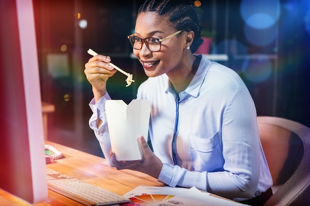 Happy businesswoman eating noodles at desk