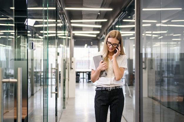 Donna di affari felice che ha conversazione piacevole del telefono. donna sorridente in camicetta bianca dell'ufficio che parla sulla cellula e che impara le buone notizie. concetto di buone notizie