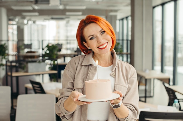 Happy businesswoman holding Birthday cake while making surprise party with her colleagues in the office