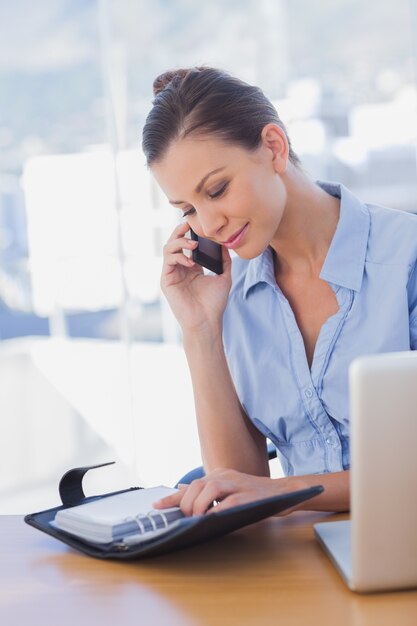 Happy businesswoman looking at her diary and calling 