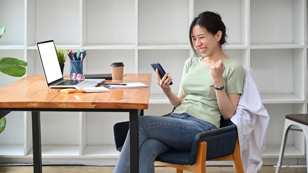 Happy businesswoman reading good news on smart phone and celebrating success