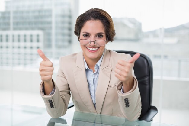 Happy businesswoman showing thumbs up at her desk