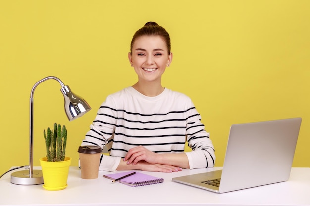 Happy businesswoman sitting in office workplace looking at camera with smile satisfied enjoying job