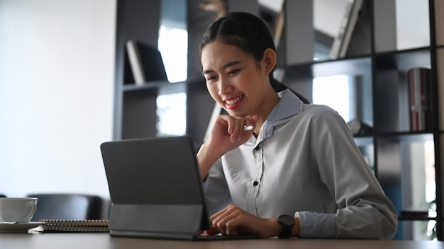 Happy businesswoman smiling and reading good news on computer tablet at office.