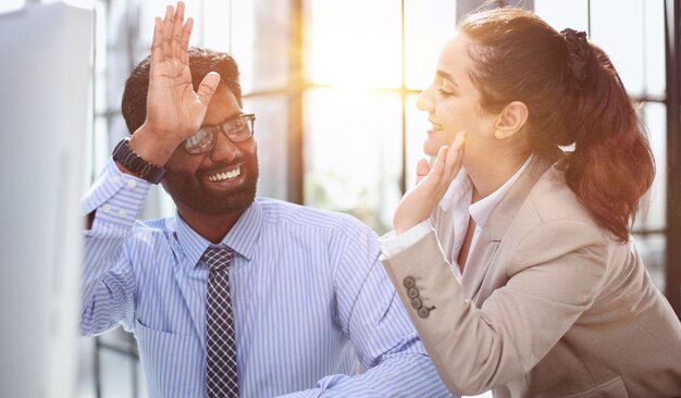 Happy businesswoman using laptop while working with colleague in the office high five