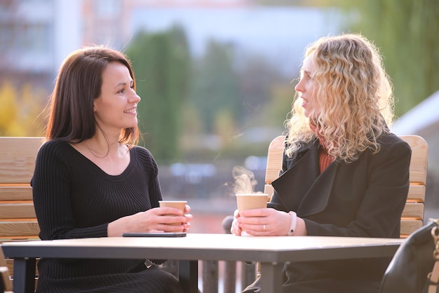 Happy businesswomen talking together during coffee break meeting at urban street cafe Friendship between business partners concept